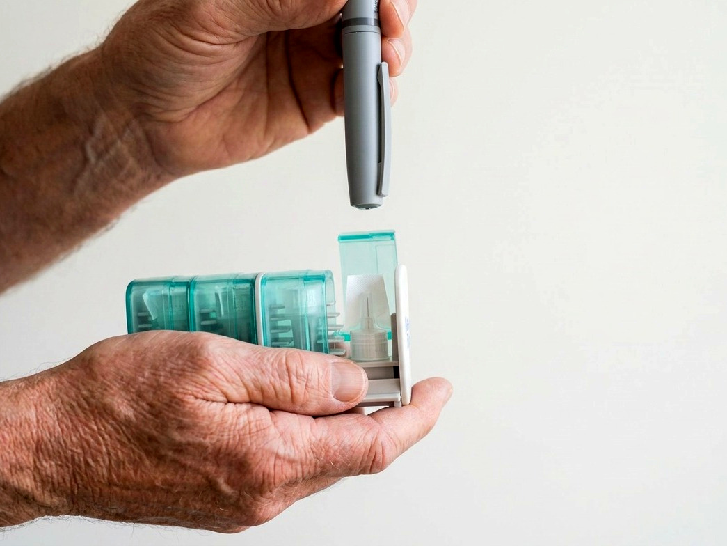 An insulin pen held above the open bay of a NeedleBay pen needle case