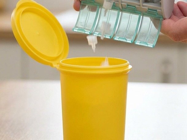 Used pen needles dropping from a NeedleBay into a yellow sharps bin